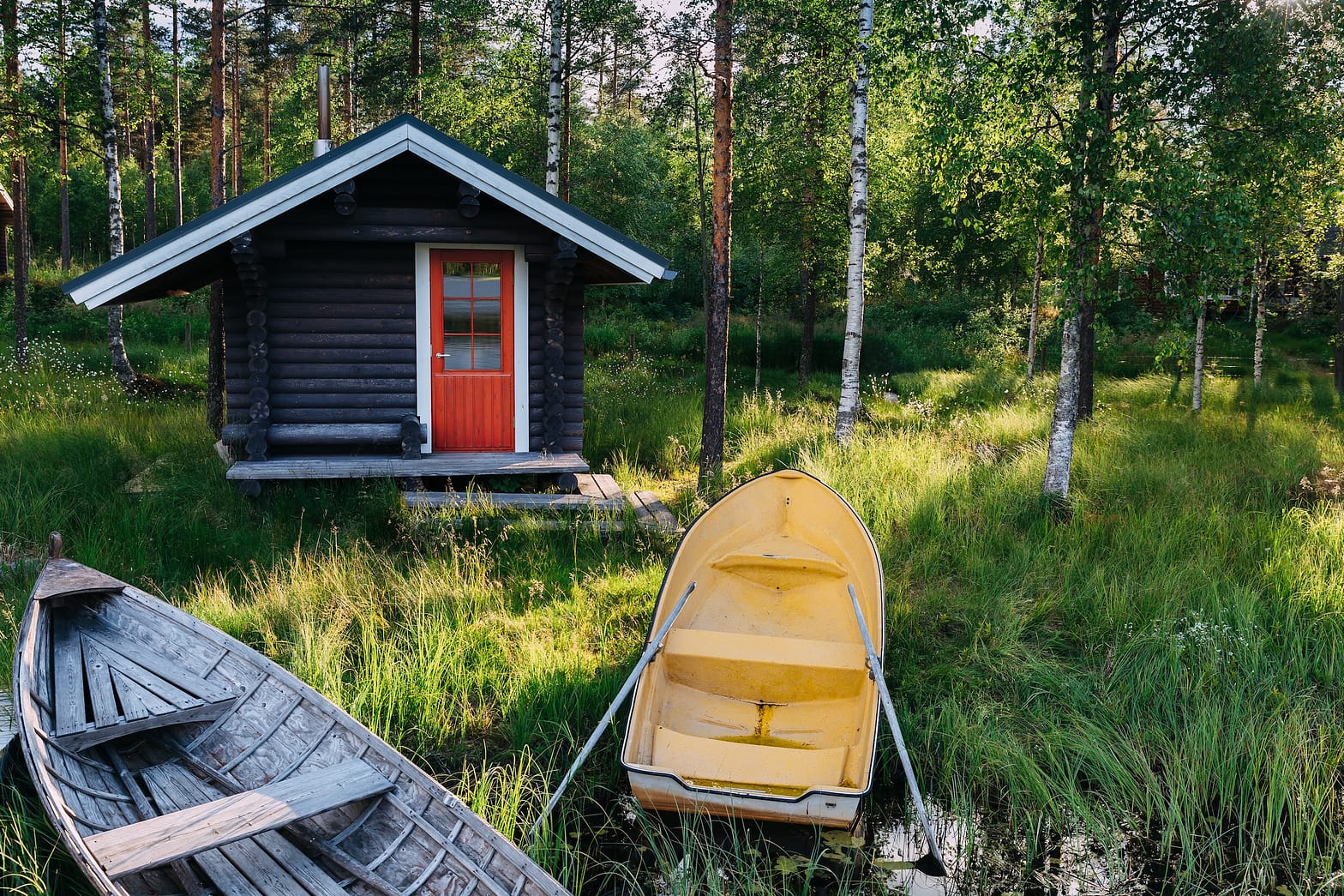 Perinteinen puinen maja. Suomalainen sauna järvellä ja laiturilla kalastusveneiden kanssa. Kesämaisema